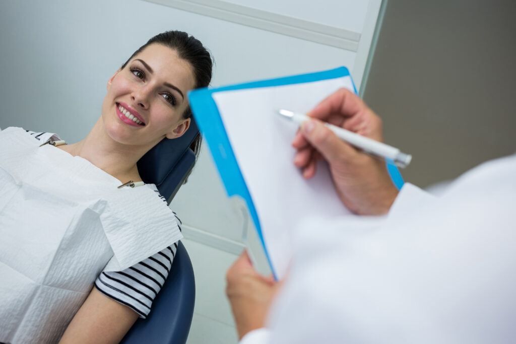 doctor writing on clipboard while patient lying on dental bed in dental clinic